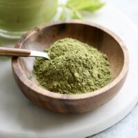 Close up view of a small wooden dish filled with green matcha powder with a spoon stuck into the powder.