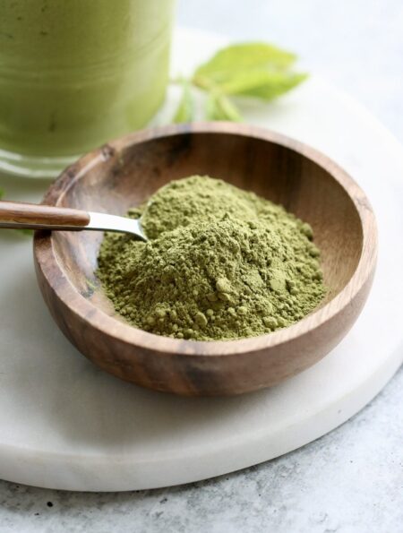 Close up view of a small wooden dish filled with green matcha powder with a spoon stuck into the powder.