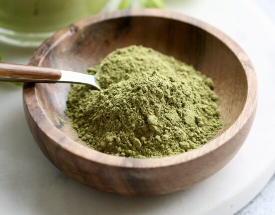 Close up view of a small wooden dish filled with green matcha powder with a spoon stuck into the powder.