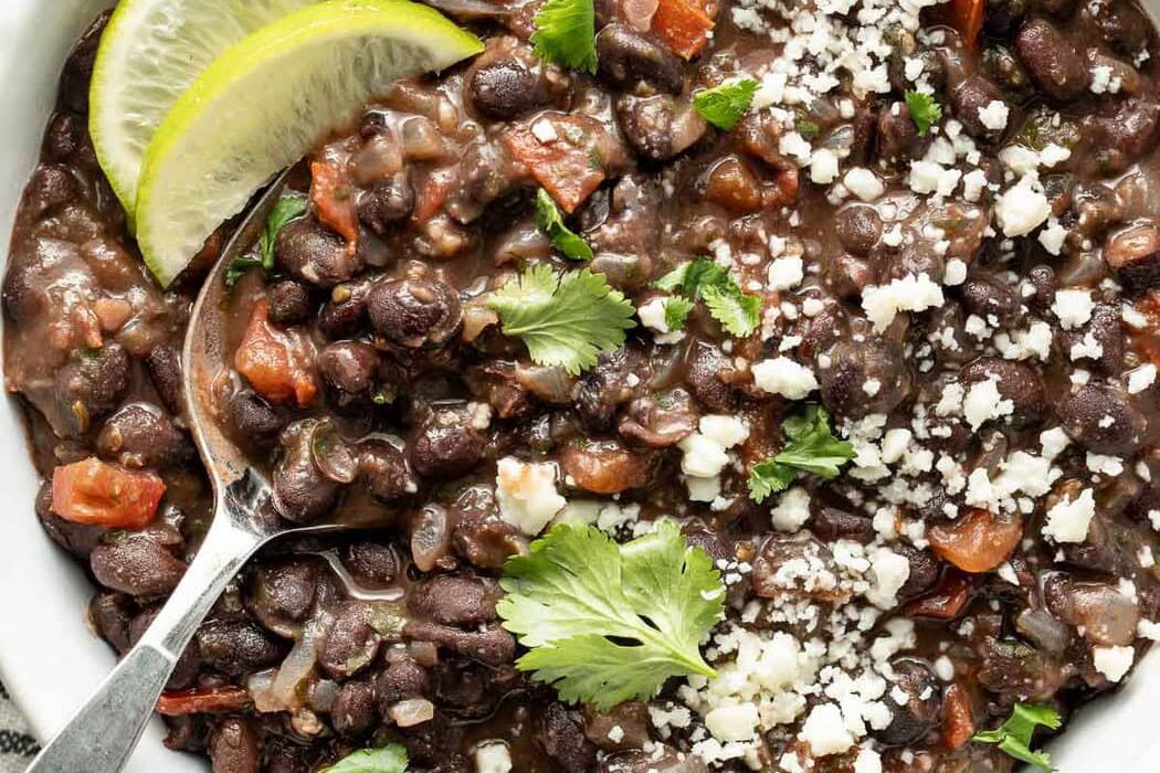 Overhead view of a bowl of Mexican Black Beans topped with fresh cilantro and garnished with lime wedges.