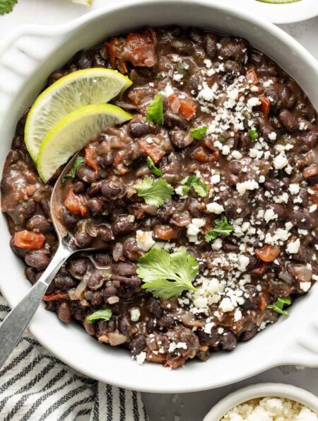 Overhead view of a bowl of Mexican Black Beans topped with fresh cilantro and garnished with lime wedges.