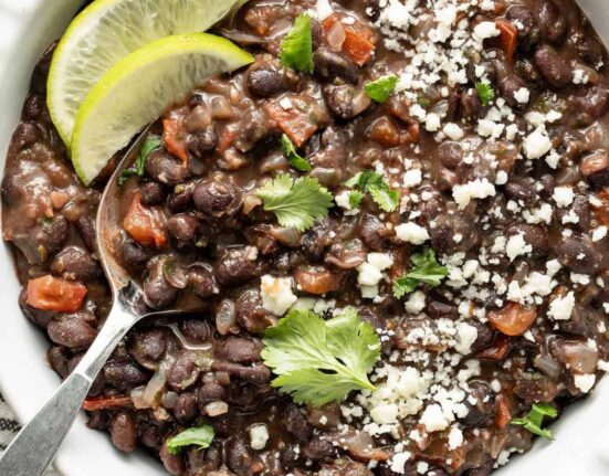 Overhead view of a bowl of Mexican Black Beans topped with fresh cilantro and garnished with lime wedges.