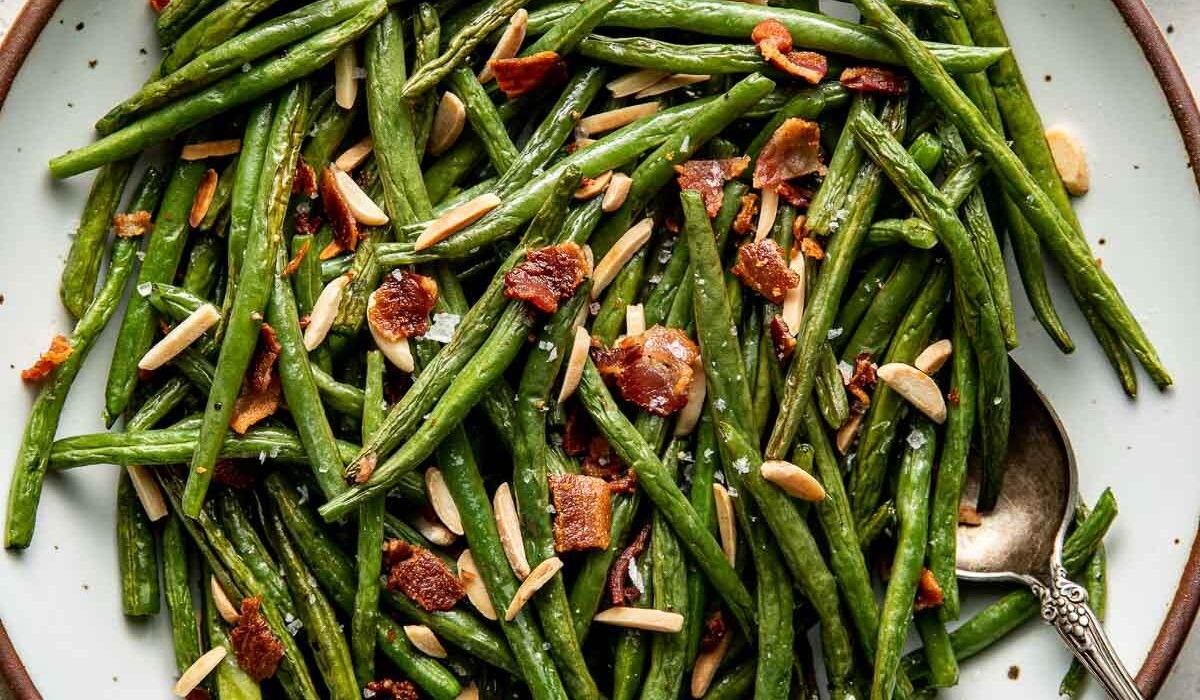 Overhead view of a plate of Roasted Green Beans topped with bacon pieces and slivered almonds.