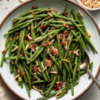 Overhead view of a plate of Roasted Green Beans topped with bacon pieces and slivered almonds.