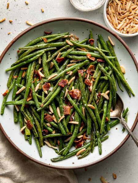 Overhead view of a plate of Roasted Green Beans topped with bacon pieces and slivered almonds.