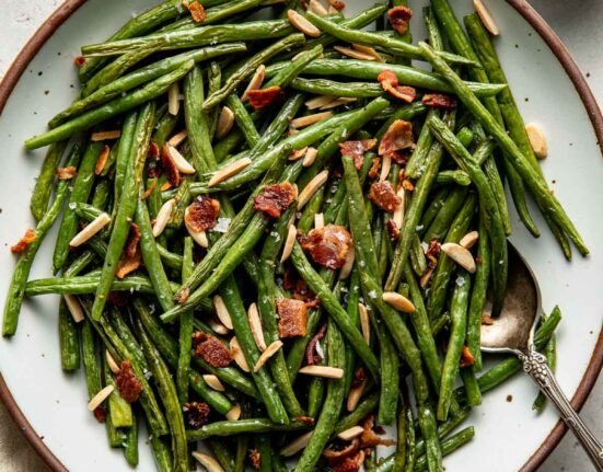 Overhead view of a plate of Roasted Green Beans topped with bacon pieces and slivered almonds.