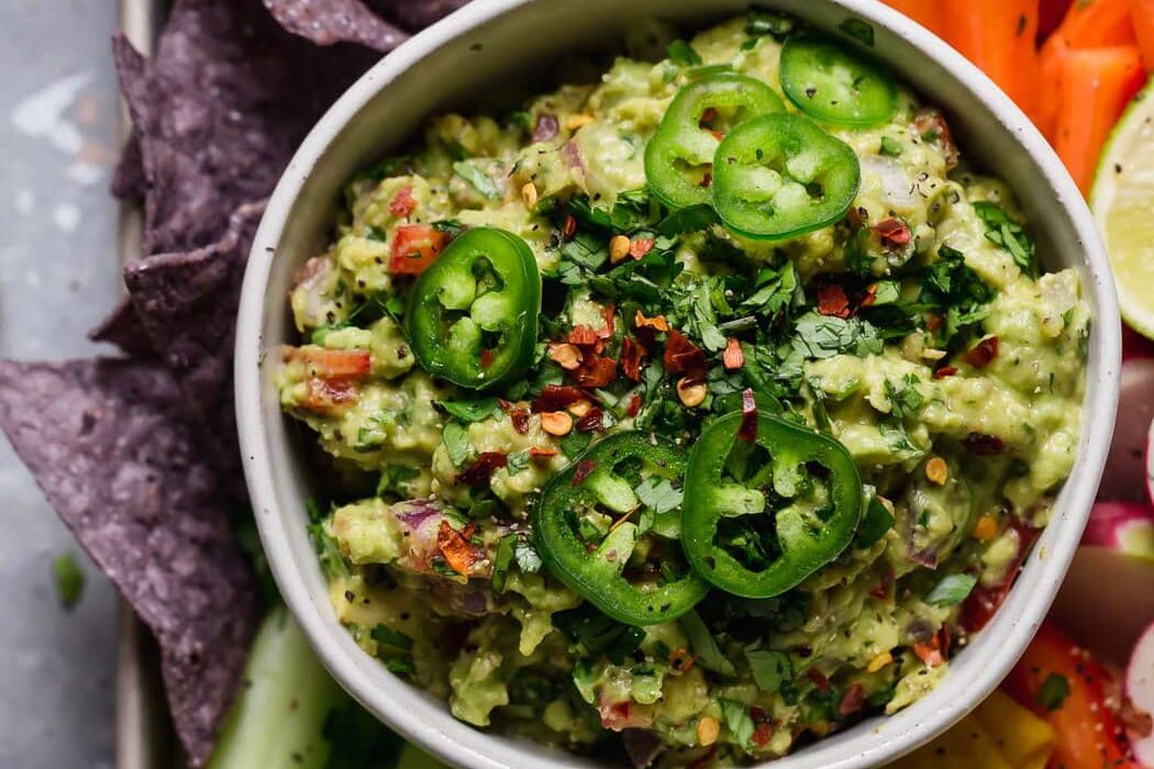 An overhead view of homemade guacamole with fresh sliced jalapenos and served with fresh veggies and tortilla chips.