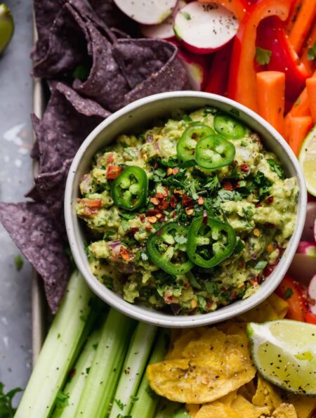 An overhead view of homemade guacamole with fresh sliced jalapenos and served with fresh veggies and tortilla chips.