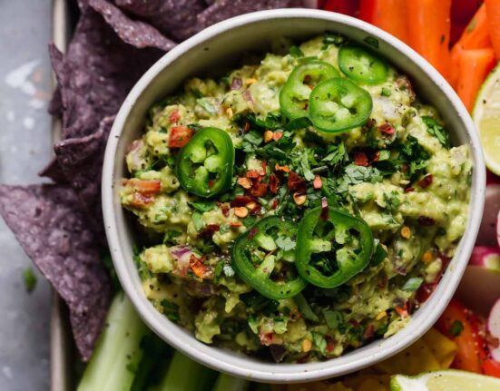 An overhead view of homemade guacamole with fresh sliced jalapenos and served with fresh veggies and tortilla chips.