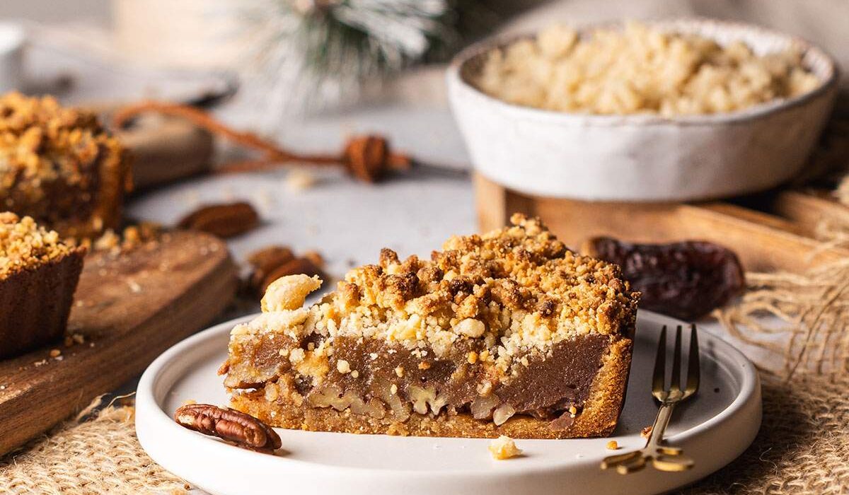 Vegan date caramel pecan tart slice on plate with crumble topping.