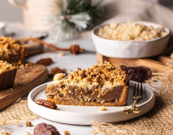 Vegan date caramel pecan tart slice on plate with crumble topping.