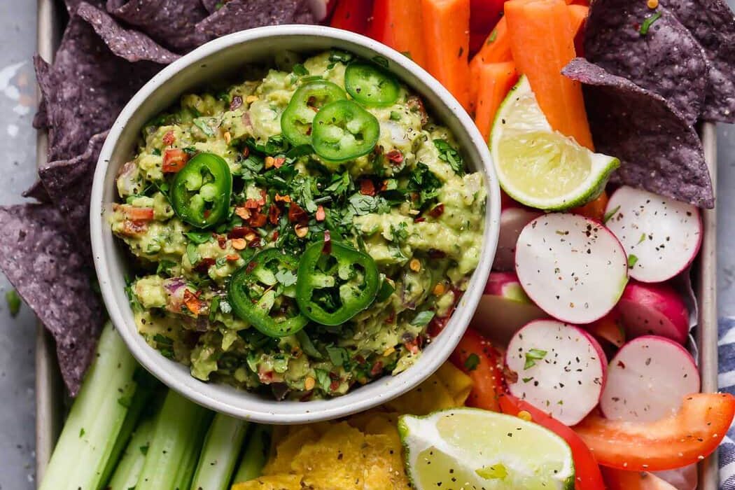 Overhead view of a bowl of fresh guacamole surrounded by freshly cut colorful veggies.