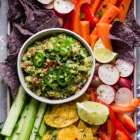 Overhead view of a bowl of fresh guacamole surrounded by freshly cut colorful veggies.