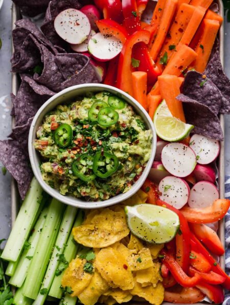Overhead view of a bowl of fresh guacamole surrounded by freshly cut colorful veggies.