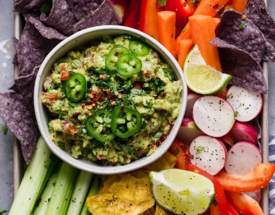 Overhead view of a bowl of fresh guacamole surrounded by freshly cut colorful veggies.