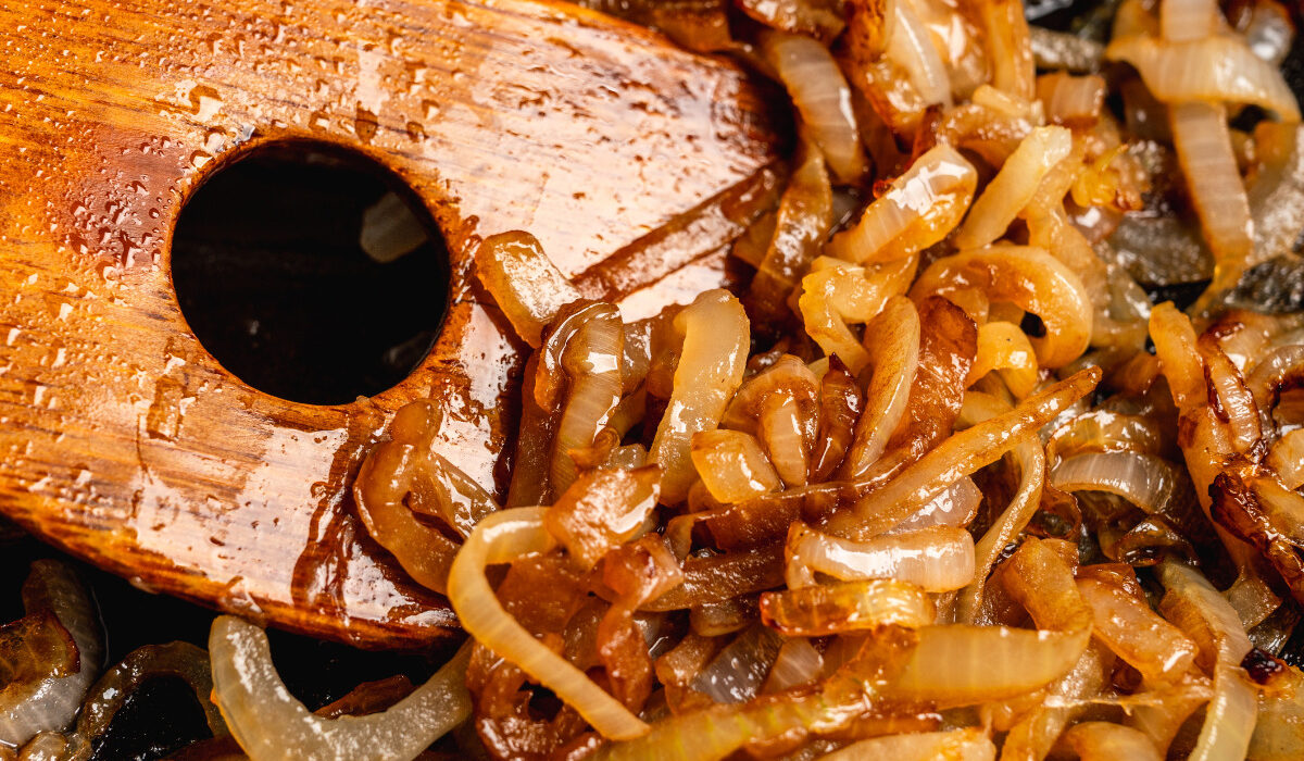 Close up image of caramelized onions being stirred with a wooden spatula