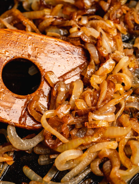 Close up image of caramelized onions being stirred with a wooden spatula