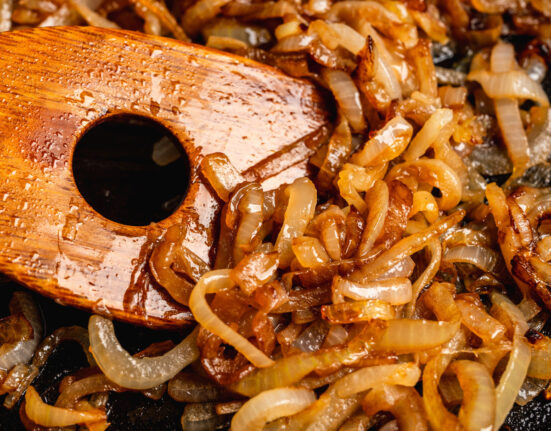 Close up image of caramelized onions being stirred with a wooden spatula