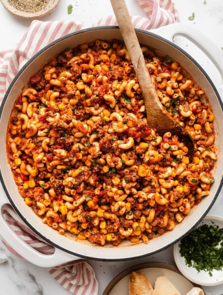 Overhead view of a skillet filled with goulash topped with fresh herbs and a wooden spoon stuck in the side.