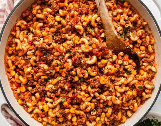 Overhead view of a skillet filled with goulash topped with fresh herbs and a wooden spoon stuck in the side.
