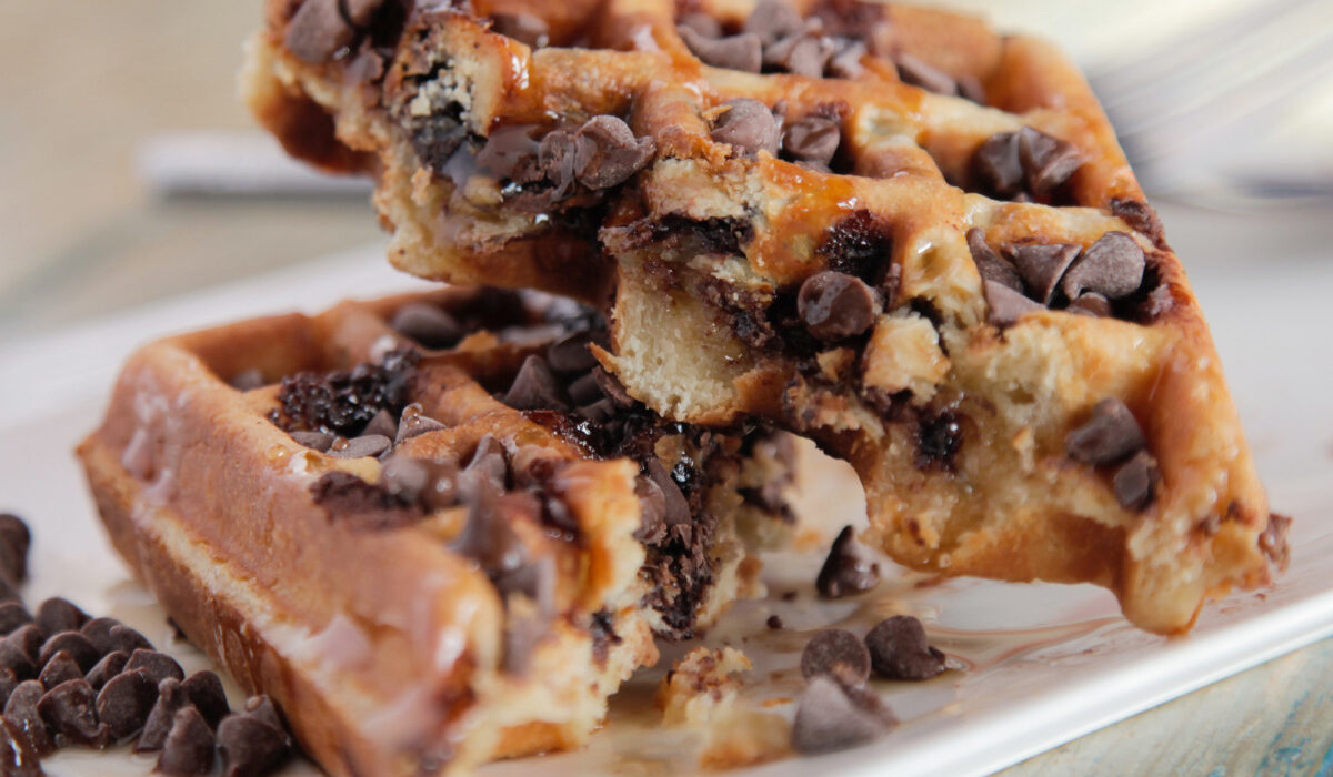 A homemade chocolate chip waffle cut in half on a plate