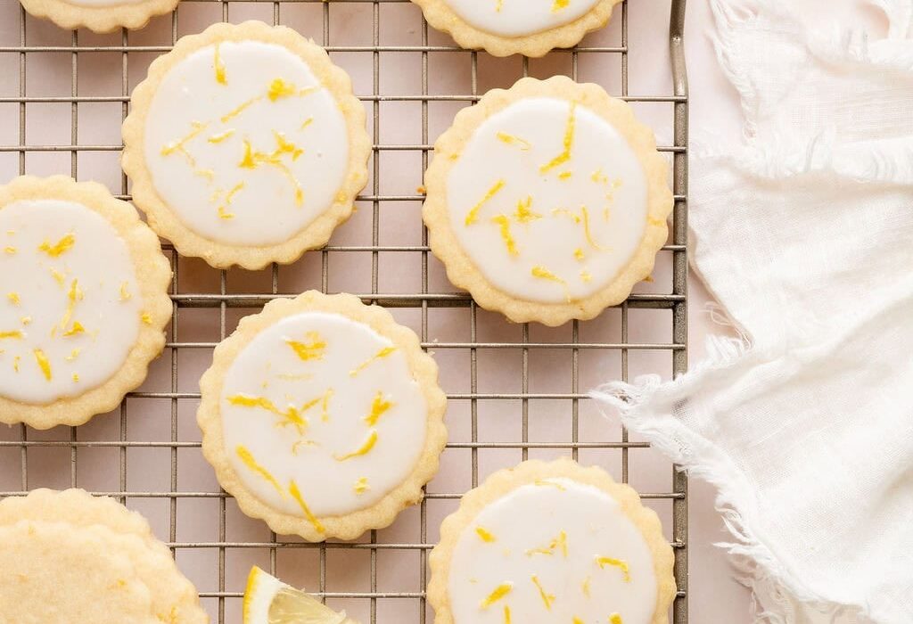Overhead view of a cooling rack filled with frosted lemon cookies sprinkled with lemon zest.