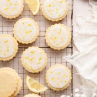 Overhead view of a cooling rack filled with frosted lemon cookies sprinkled with lemon zest.
