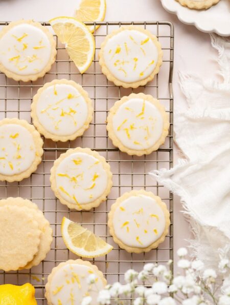Overhead view of a cooling rack filled with frosted lemon cookies sprinkled with lemon zest.