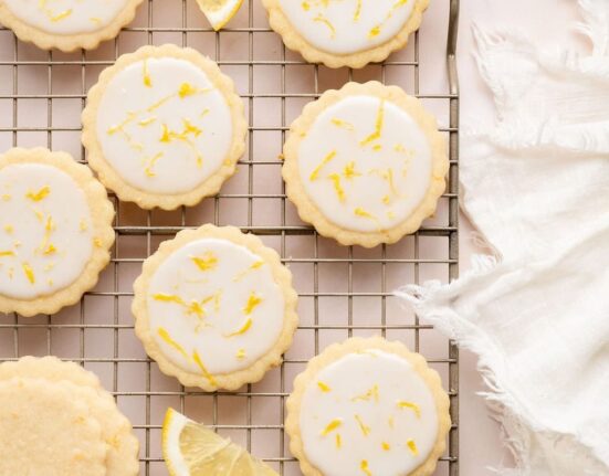 Overhead view of a cooling rack filled with frosted lemon cookies sprinkled with lemon zest.