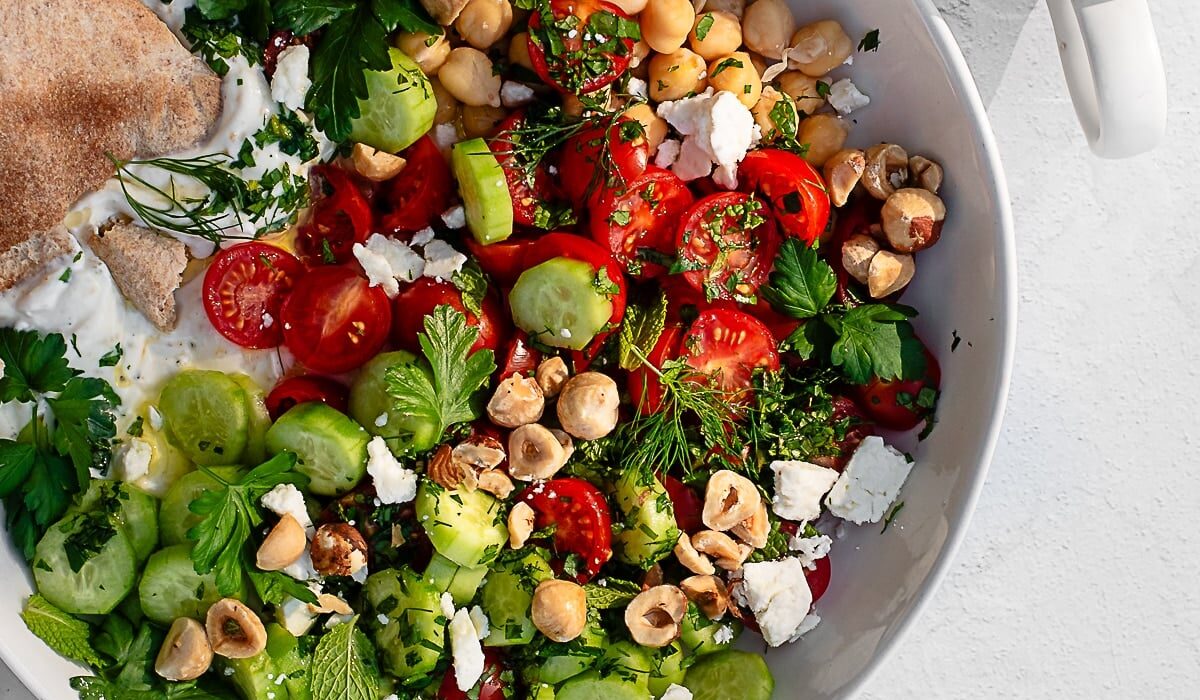 savory yogurt bowl garnished with feta, herbs and hazelnuts in a white bowl on a white surface