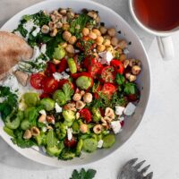 savory yogurt bowl garnished with feta, herbs and hazelnuts in a white bowl on a white surface