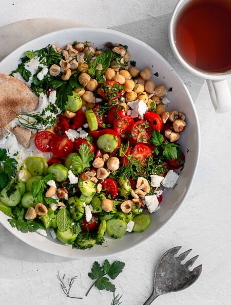 savory yogurt bowl garnished with feta, herbs and hazelnuts in a white bowl on a white surface