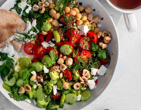 savory yogurt bowl garnished with feta, herbs and hazelnuts in a white bowl on a white surface