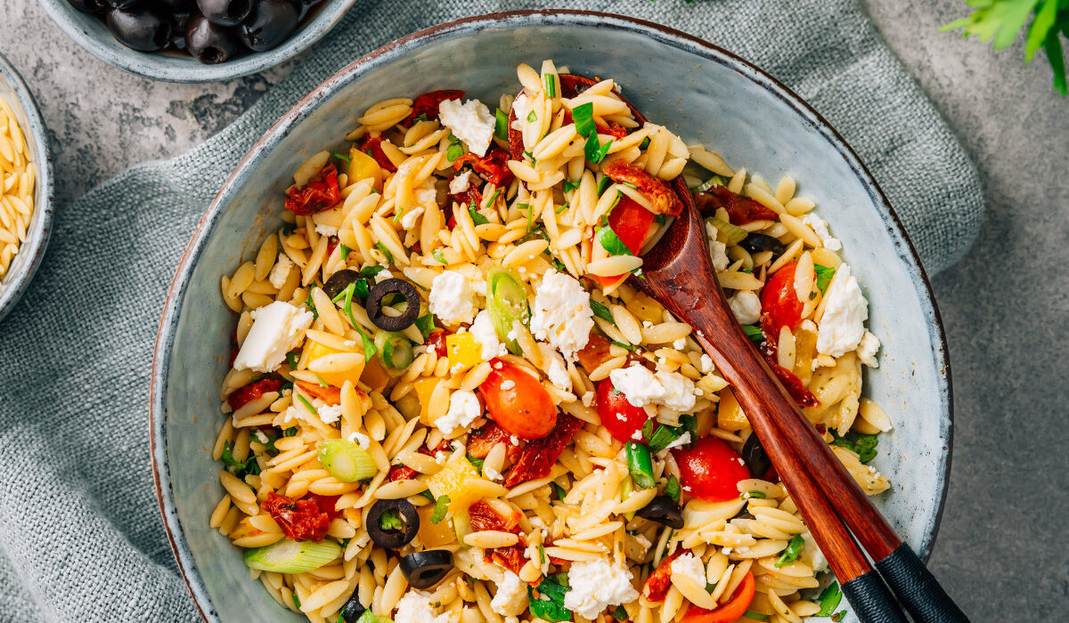 Overhead image of Orzo Salad in a bowl with serving spoons