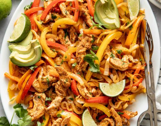 Overhead view of a platter filled with Chicken Fajitas and garnished with avocado, limes, and cilantro.