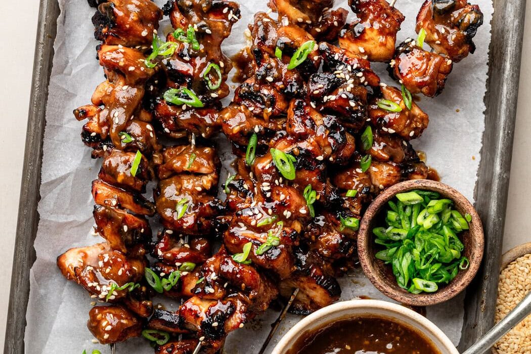 Overhead view of a sheet pan of Korean BBQ chicken skewers topped with green onions and sesame seeds.
