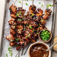 Overhead view of a sheet pan of Korean BBQ chicken skewers topped with green onions and sesame seeds.