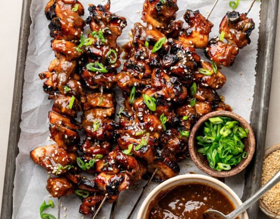 Overhead view of a sheet pan of Korean BBQ chicken skewers topped with green onions and sesame seeds.