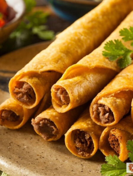 CLose up image of air fryer taquitos stacked on a plate with cilantro and salsa in the background