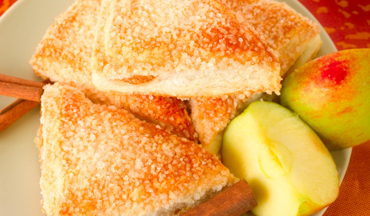 Overhead image of Apple Turnovers on a plate with cinnamon sticks and sliced apple