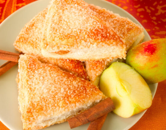 Overhead image of Apple Turnovers on a plate with cinnamon sticks and sliced apple