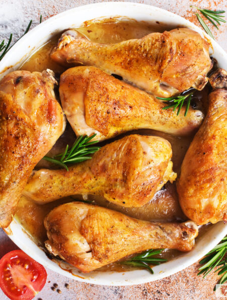 overhead image of crispy baked chicken legs in a white dish with herbs