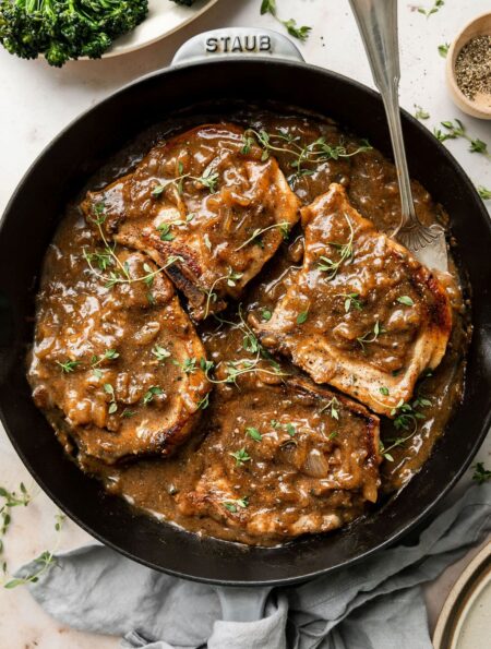 Overhead view of a cast iron pan filled with The Best Smothered Pork Chops topped with fresh herbs and brown gravy.
