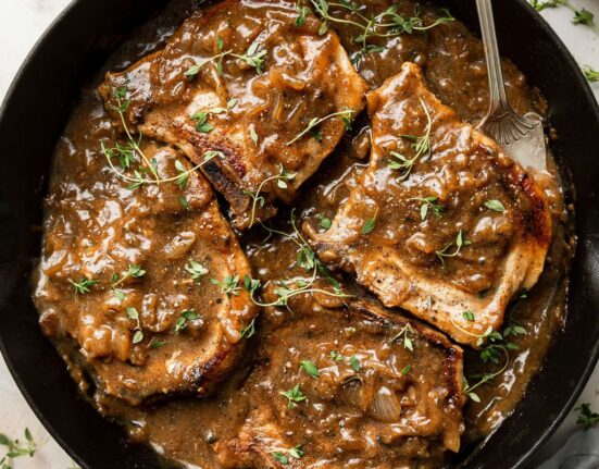 Overhead view of a cast iron pan filled with The Best Smothered Pork Chops topped with fresh herbs and brown gravy.