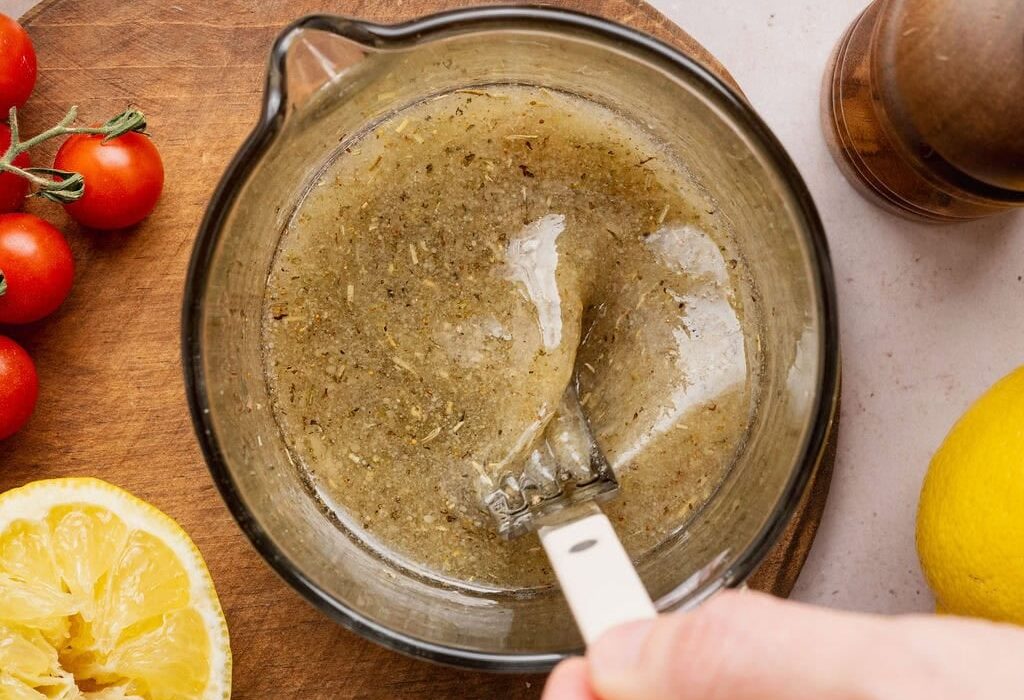 Overhead view of a hand stirring an Italian Dressing mixture in a measuring glass.