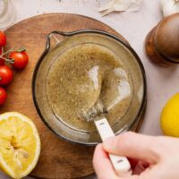 Overhead view of a hand stirring an Italian Dressing mixture in a measuring glass.