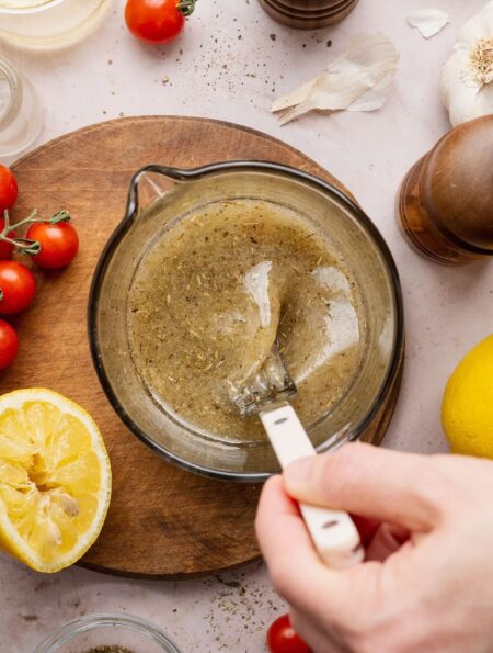Overhead view of a hand stirring an Italian Dressing mixture in a measuring glass.