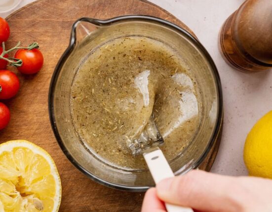 Overhead view of a hand stirring an Italian Dressing mixture in a measuring glass.