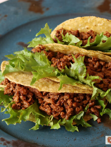 Three crunchy tacos with Instant Pot Taco Meat and lettuce on a blue plate