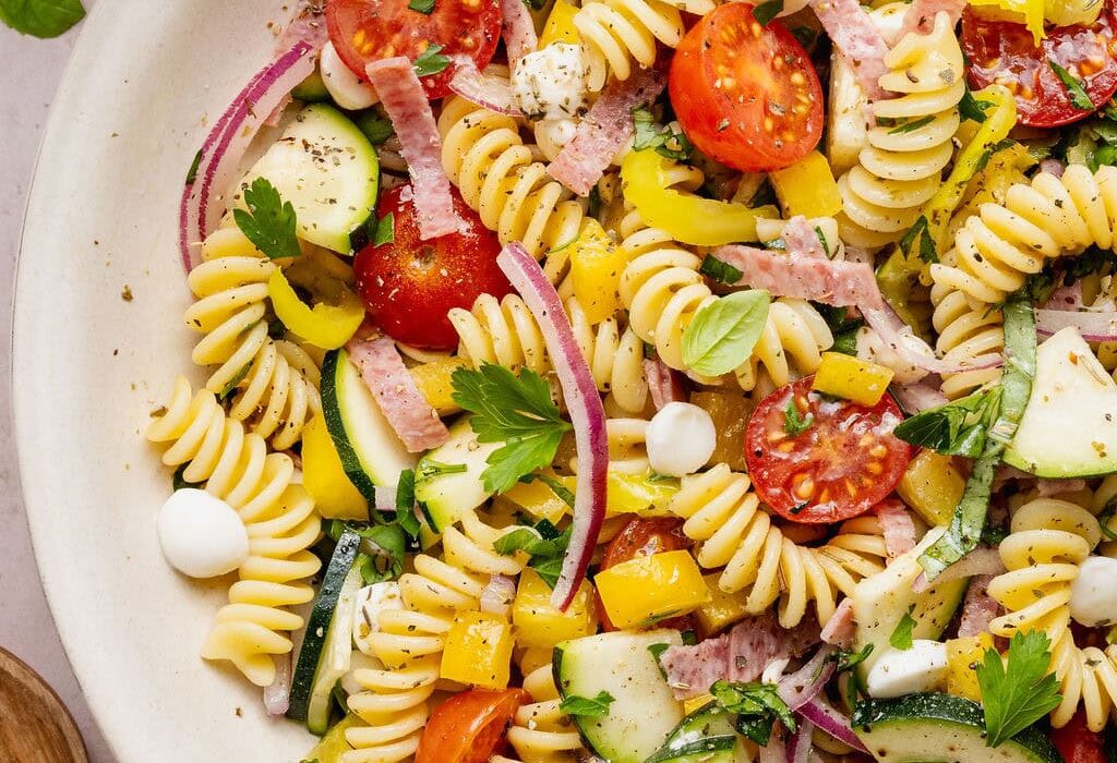 Overhead view of a colorful Zesty Italian Pasta Salad topped with fresh herbs and black pepper.